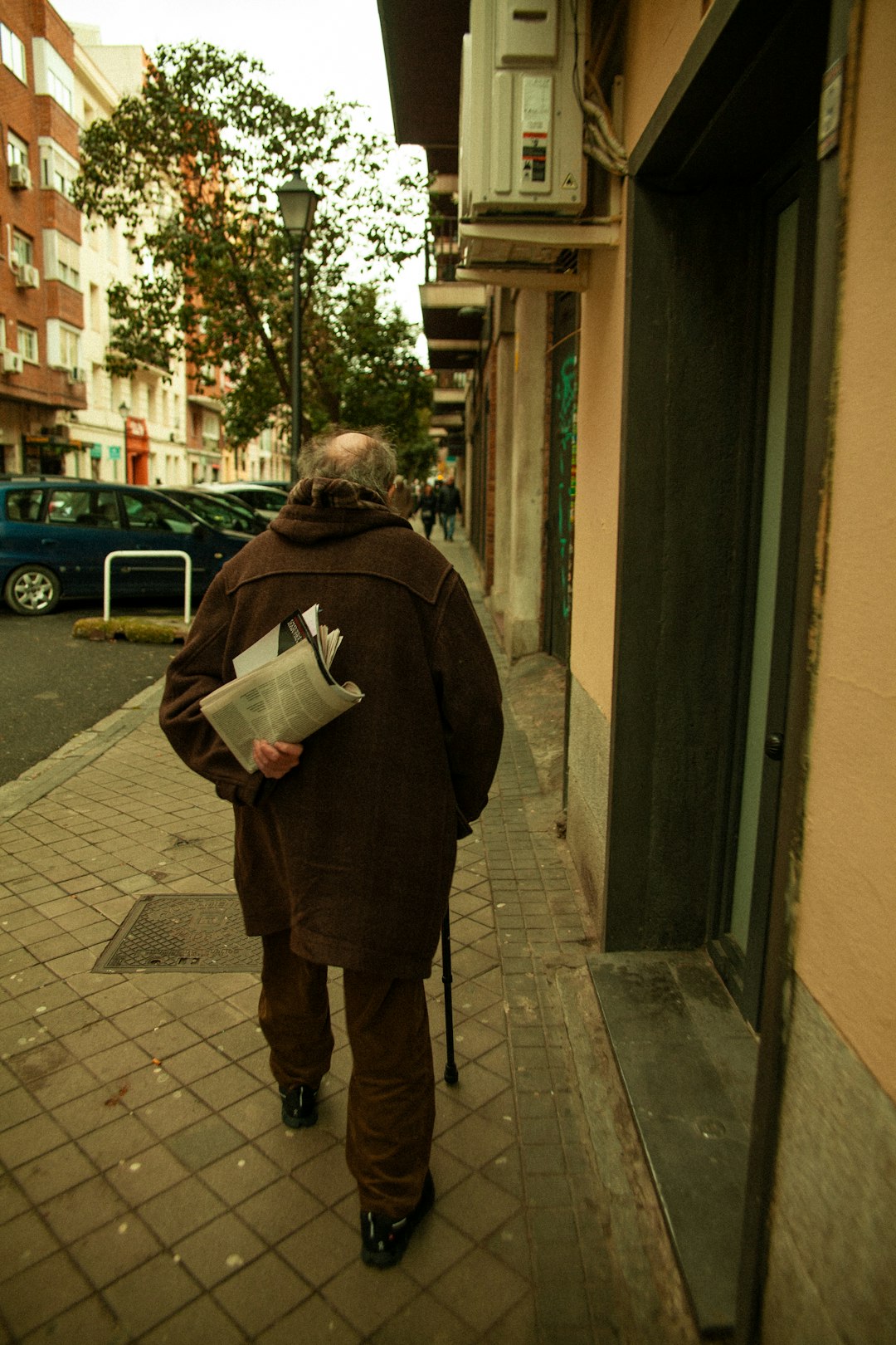 senior-man-walking-on-a-sidewalk-holding-a-newspaper-0irlb-fhj1w
